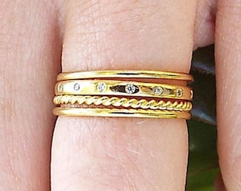 Puede incluir: Un conjunto de cuatro anillos apilables de oro con una fina banda de diamantes en el anillo superior.