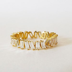 May include: A gold ring with a row of clear baguette-shaped stones.