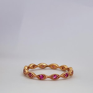 May include: A gold band ring with a delicate design featuring a row of pink gemstones.