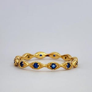 Op de afbeelding: Een gouden bandring met een delicaat, gegolfd ontwerp en kleine blauwe edelstenen.