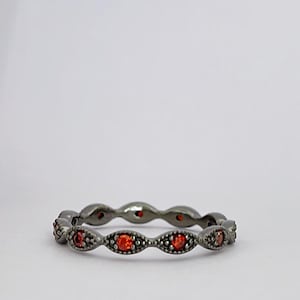 May include: A black band ring with a wavy design and small red gemstones.