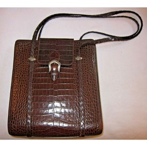 Pu&ograve; includere: Una borsa a mano in pelle marrone con motivo coccodrillo e fibbia argentata. La borsa ha una tracolla intrecciata.