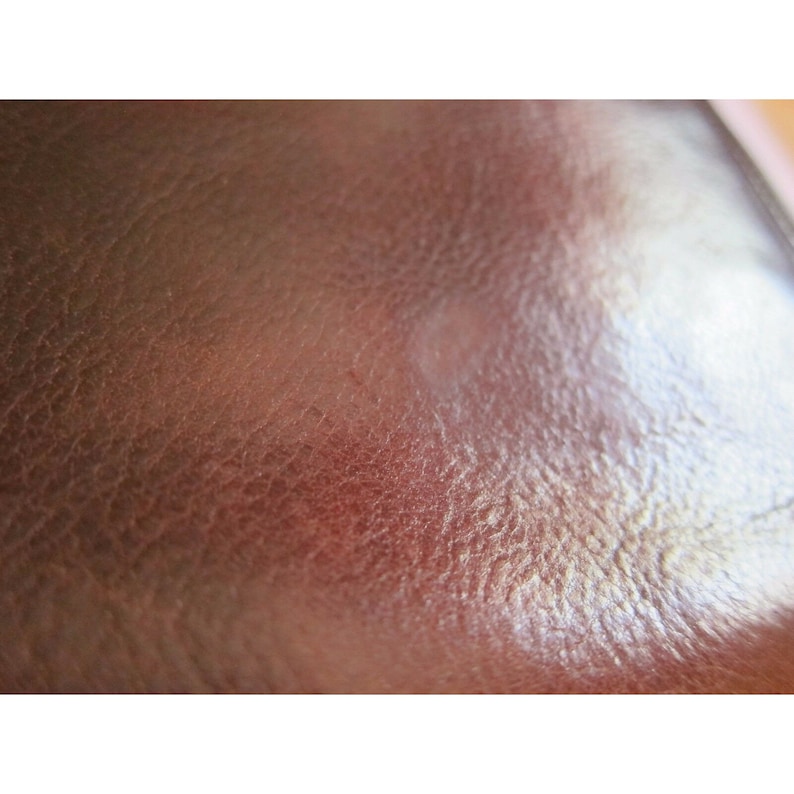 Pu&ograve; includere: Primo piano di una superficie in pelle marrone con una grana testurizzata. La pelle ha una leggera lucentezza e sembra essere morbida e flessibile.