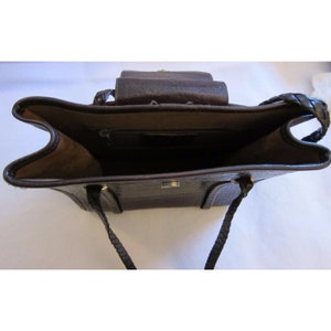 Pu&ograve; includere: Una borsa a mano in pelle marrone con una tracolla intrecciata e una chiusura a lembo. La borsa ha una tasca con cerniera all'interno.