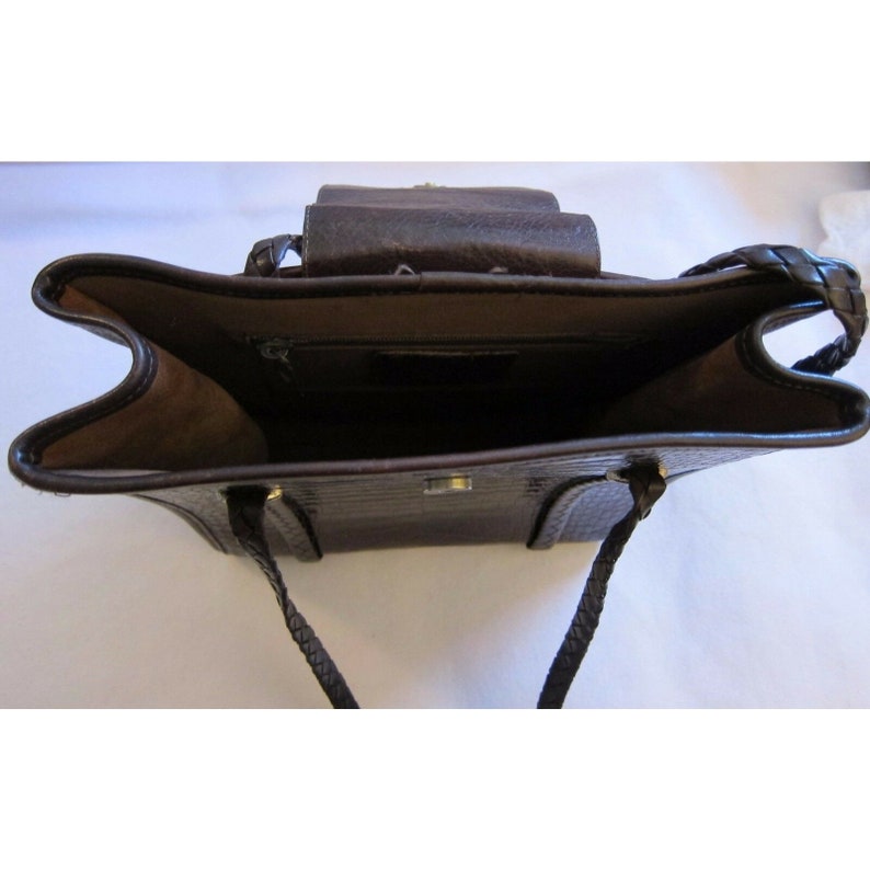 Pu&ograve; includere: Una borsa a mano in pelle marrone con una tracolla intrecciata e una chiusura a lembo. La borsa ha una tasca con cerniera all'interno.