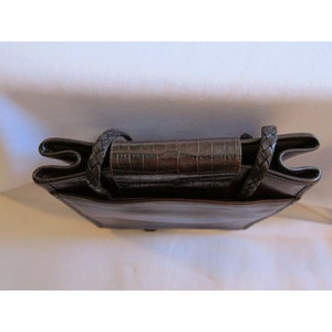 Pu&ograve; includere: Una borsa a mano in pelle marrone con una tracolla intrecciata e una patta con effetto coccodrillo.