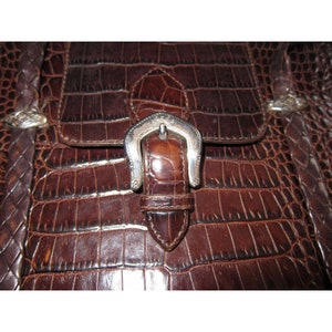 Pu&ograve; includere: Primo piano di una borsa di pelle marrone con una fibbia argentata. La borsa ha un motivo a pelle di coccodrillo.