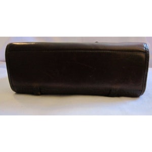 Pu&ograve; includere: Una borsa a mano in pelle marrone scuro con una finitura liscia. La borsa ha una forma rettangolare e una leggera lucentezza.