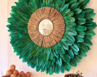 May include: A circular wall mirror featuring a central glass pane surrounded by a thick, radiating border of natural tan raffia fibers, which is further encircled by multiple dense layers of vibrant emerald green feathers in a sunburst pattern.