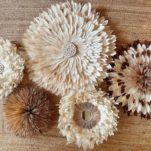 Peut inclure: Cinq décorations murales avec une esthétique naturelle et organique. Les pièces présentent une variété de textures et de couleurs, notamment crème, marron et beige. Les motifs ressemblent à des fleurs ou à des éclats de soleil, ajoutant une touche de décoration inspirée de la nature.