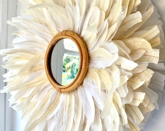 May include: A round mirror with a woven frame surrounded by white and cream feathers.