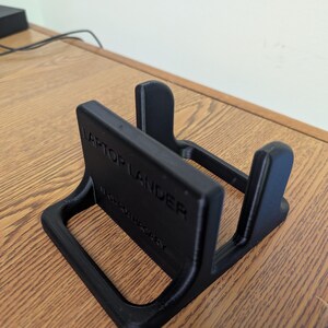 May include: Black plastic laptop stand with the text "Laptop Lander" printed on the side.