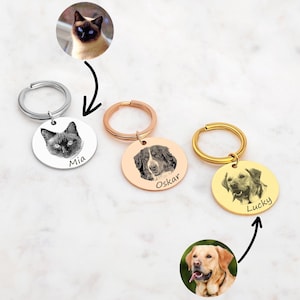 Può includere: Tre portachiavi in argento, oro rosa e oro con incisioni fotografiche personalizzate. I portachiavi raffigurano un gatto nero, un cane bianco e nero e un golden retriever. I portachiavi sono etichettati "Mia", "Oskar" e "Lucky".