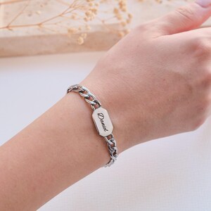 K&ouml;nnte beinhalten: Silberfarbenes Armband mit Kettengliedern und einem rechteckigen Namensschild. Auf dem Schild steht der Name "Daniel" in Schreibschrift. Das Armband wird am Handgelenk getragen.
