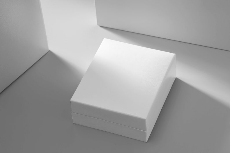 K&ouml;nnte beinhalten: Eine wei&szlig;e quadratische Box mit Deckel, die auf einer grauen Oberfl&auml;che steht. Die Box ist scharf, der Hintergrund unscharf.