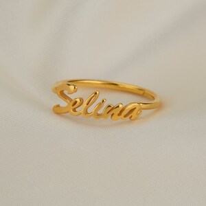 May include: A gold-coloured ring with the name "Selina" written in a cursive script.