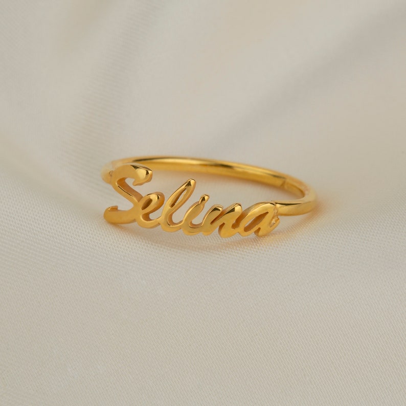May include: A gold-coloured ring with the name "Selina" written in a cursive script.