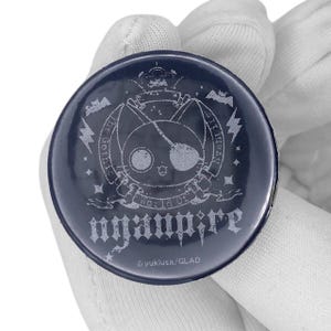 May include: A dark blue round button with a cat illustration wearing an eyepatch, a crown, and the text "nyaupire". The button also features the text "The Gothic World of Nyaupire" and the copyright information.