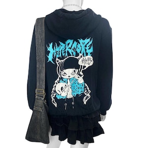May include: Black hoodie with a graphic print of a cartoon character with the text "HYPERCORE" and "地獄ガール" on the back. The hoodie has a drawstring hood and a zipper closure.
