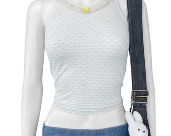 May include: White tank top with a dotted pattern and lace trim around the neckline. A small yellow bow is attached to the lace. The top is paired with denim shorts and a dark denim shoulder bag. A white stuffed bunny is attached to the bag.