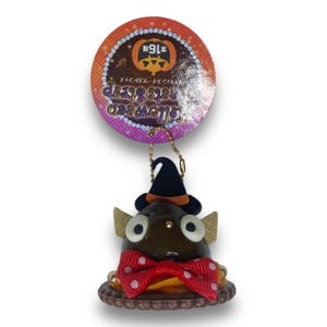 May include: A brown and black Halloween-themed character charm with large eyes, a witch's hat, and a red bow with white polka dots. The charm is attached to a gold chain and has a tag that reads "Halloween  Get's Spooky  ¥198".