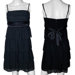 May include: A black tiered dress with a satin ribbon around the waist. The dress has a square neckline and thin straps.