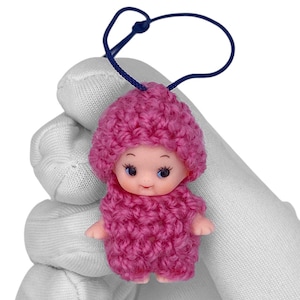 May include: A small pink crocheted doll with a pink hat and a blue cord attached to the top of the hat.