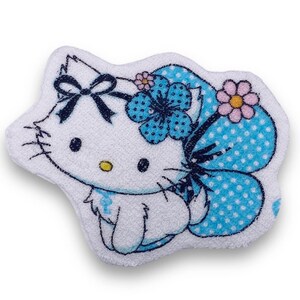 May include: A white plush bath sponge shaped like Hello Kitty. The sponge has blue and white polka dot accents and a blue flower with white polka dots.