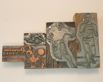 May include: Five vintage wood printing blocks with metal type. The blocks feature images of a person playing basketball, a person playing football, a person skateboarding, a person bowling, and the text "LANES RECREATION".