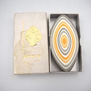May include: Vintage playing cards in a box. The card design features concentric ovals in orange, gray, and white. The box is off-white with a gold spade emblem and text.
