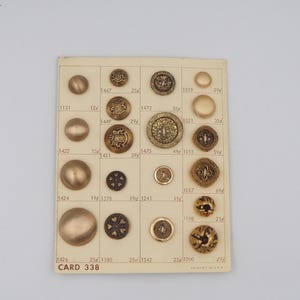 May include: A collection of vintage brass buttons of various sizes and designs, arranged on a card. The card is labeled "CARD 338" and features buttons with ornate patterns and textures, perfect for sewing or crafting.