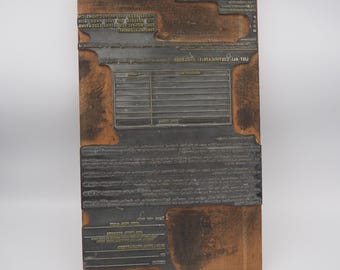 Peut inclure: Un bloc d'impression vintage avec des caractères métalliques encastrés dans une base en bois. Le bloc présente divers éléments textuels et une section en forme de grille, probablement pour des formulaires ou des tableaux. Le type métallique est sombre, contrastant avec le bois.