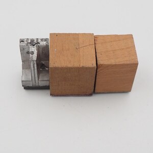 May include: An image of a metal and wood object. The object is composed of three parts: a silver metal piece and two wooden blocks. The wooden blocks are a light brown color. The metal piece is a darker silver color.