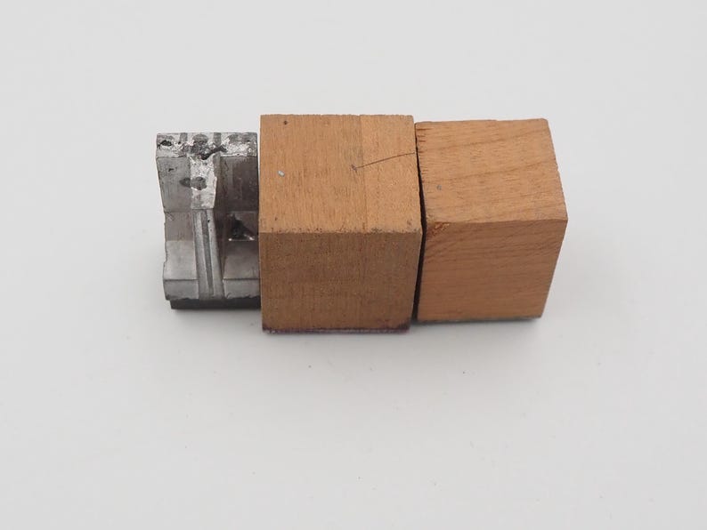 May include: An image of a metal and wood object. The object is composed of three parts: a silver metal piece and two wooden blocks. The wooden blocks are a light brown color. The metal piece is a darker silver color.