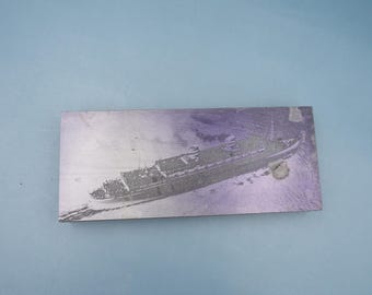 May include: A rectangular, grayscale image of a ship at sea. The ship is depicted in detail, with visible decks, structures, and a wake. The background is a light, textured surface.