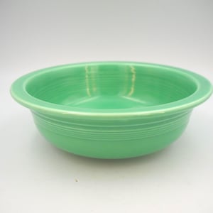 May include: A light green ceramic bowl with a rounded rim and a slightly flared base. The bowl has horizontal ridges around the exterior and a smooth interior. The bowl is empty and sits on a white surface.