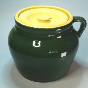 May include: A green ceramic bean pot with a yellow lid and a handle. The pot has a rounded shape and a smooth, glossy finish.
