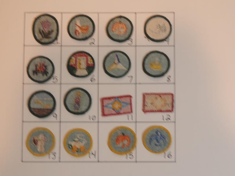 Op de afbeelding: Een wit vel papier met 16 ronde plekken, elk met een ander ontwerp, erop genaaid. De plekken zijn genummerd van 1 tot en met 16. De plekken zijn allemaal in verschillende kleuren en ontwerpen, waaronder een pompoen, een huis, een vogel, een bloem en een zeilboot.