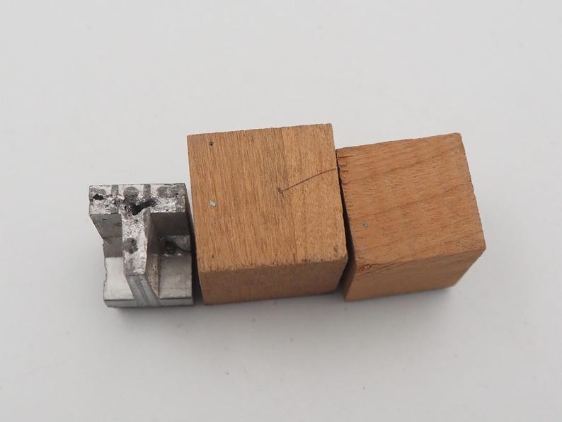 May include: An assortment of small wooden and metal blocks. Two square wooden blocks are side by side, with a third, smaller, metal block to the left. The wood is a light brown color, and the metal block is silver.