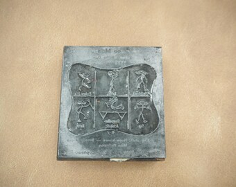 May include: A rectangular, gray metal printing block with a curved central design. The block features six small, stylized figures and text. The figures are arranged in a grid, and the text appears to be in a foreign language.