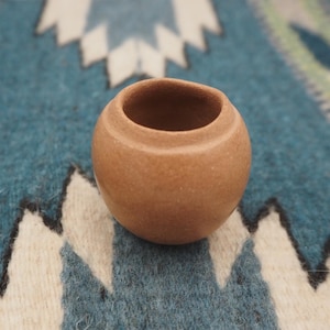 以下が含まれることがあります： 丸みを帯びたテラコッタ色の小さなセラミック容器で、広い開口部があります。陶器は滑らかで無釉の表面とシンプルでミニマルなデザインです。この容器はおそらく手作りで、小さな植物や装飾目的などに適しています。