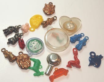Op de afbeelding: Een verzameling vintage plastic bedels, waaronder een hartvormige bedel met een klokje, een blauwe hartbedel, een rode zeehondbedel, een groene hertbedel, een rood-gouden leeuwenbedel, een groen-witte cartoonbedel, een zilveren panbedel, een rode autobedel, een doorzichtige plastic bedel met een zeemeermin erin, een blauw-witte figuurbedel, een roze varkenbedel, een gele katbedel, een rood-gouden figuurbedel, een blauw-witte figuurbedel en een gouden figuurbedel.