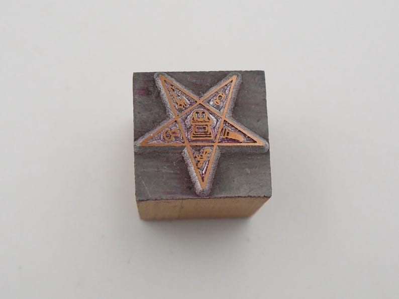 May include: A vintage wood and metal stamp featuring a five-pointed star design. The star has an intricate pattern with copper-colored details. The stamp is rectangular, with the star design centered on the top surface.