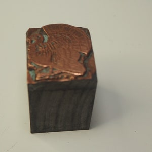 K&ouml;nnte beinhalten: Ein vintage Druckblock aus Metall mit einem erhabenen Bild eines Truthahns. Der Block ist aus Holz und hat eine kupferfarbene Oberfl&auml;che.