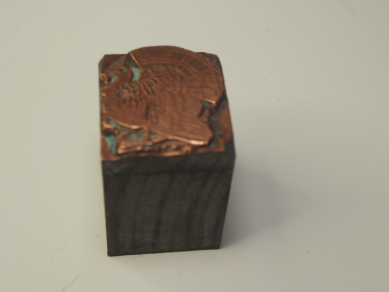 K&ouml;nnte beinhalten: Ein vintage Druckblock aus Metall mit einem erhabenen Bild eines Truthahns. Der Block ist aus Holz und hat eine kupferfarbene Oberfl&auml;che.