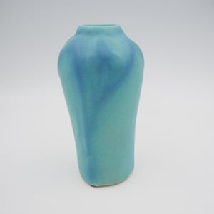 May include: A turquoise ceramic vase with a unique, organic shape. The vase has a smooth, matte finish and a darker blue accent that flows down the front. The vase is approximately 6 inches tall and is suitable for displaying flowers or as a decorative piece.