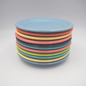 Pode incluir: Uma pilha de pratos de cerâmica coloridos em várias tonalidades, incluindo azul claro, laranja, amarelo, rosa, preto, verde-azulado e verde. Os pratos têm um design clássico e simples com uma borda ligeiramente elevada.