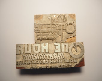 May include: Two vintage wooden printing blocks with metal type. The top block reads "City Elite" with an illustration of a city skyline. The bottom block reads "More Than Dry Cleaning" and "One Hour Martinis" with a stylized illustration of a martini glass.
