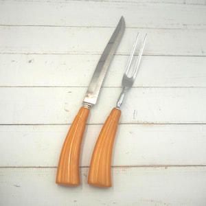 Può includere: Un set da intaglio vintage con manici in plastica arancione. Il set comprende un coltello e una forchetta.