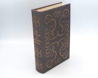 May include: A hardcover book titled "The Confessions of Jean-Jacques Rousseau." The dark brown cover features gold decorative swirls and the title in gold lettering. The book's pages are visible at the top.